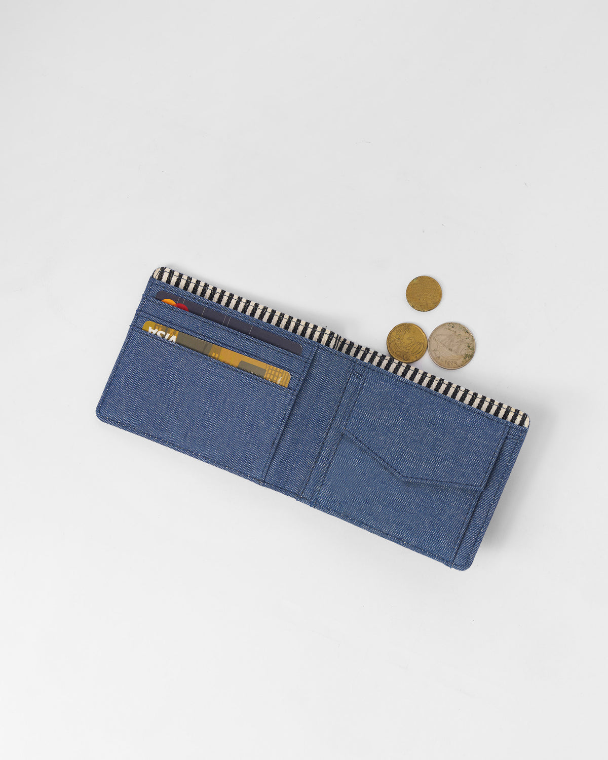 Open denim blue Classic Bi-Fold Wallet holding cards with coins beside it.