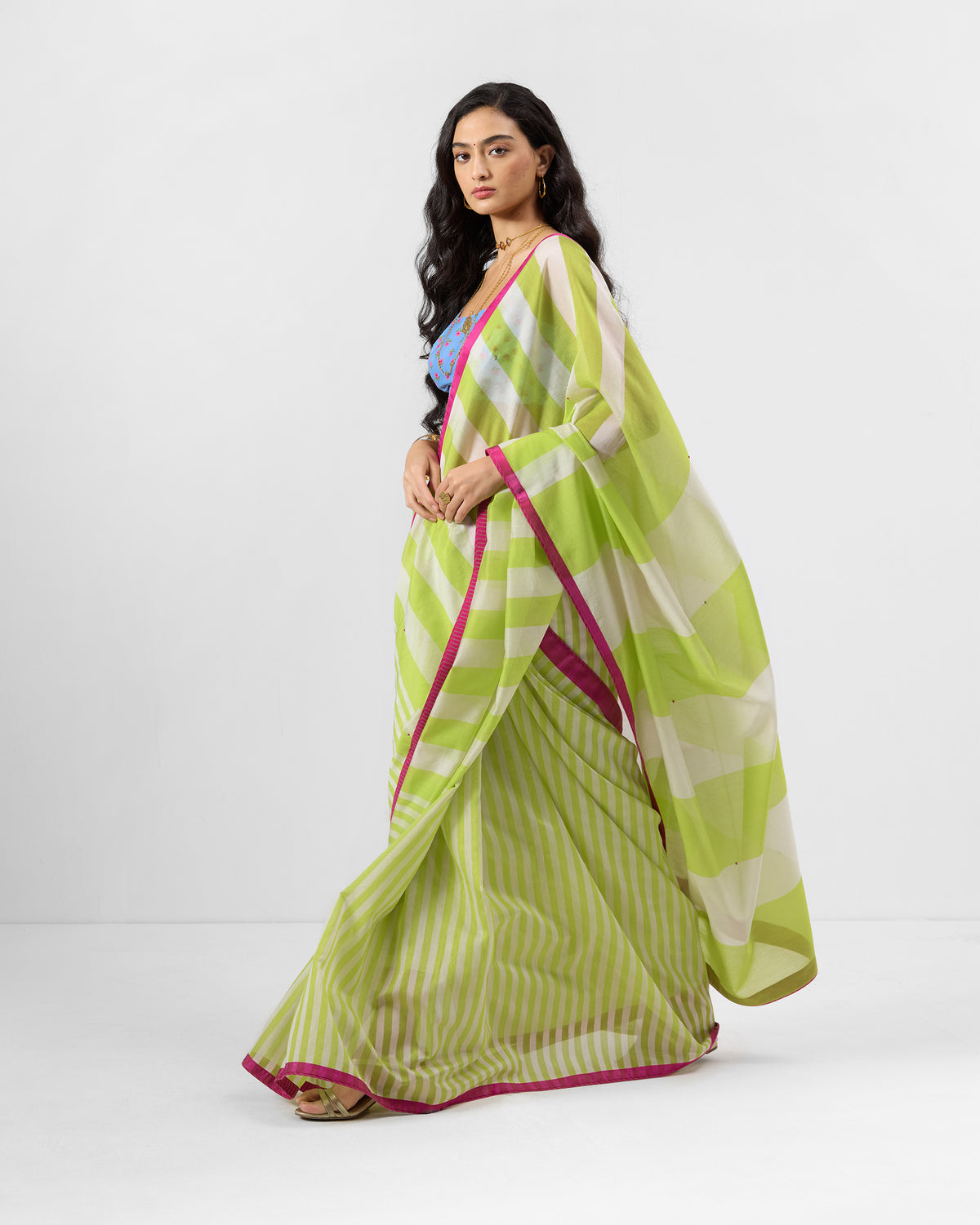 Person wearing a lime and ivory striped Veha sari with a magenta border.