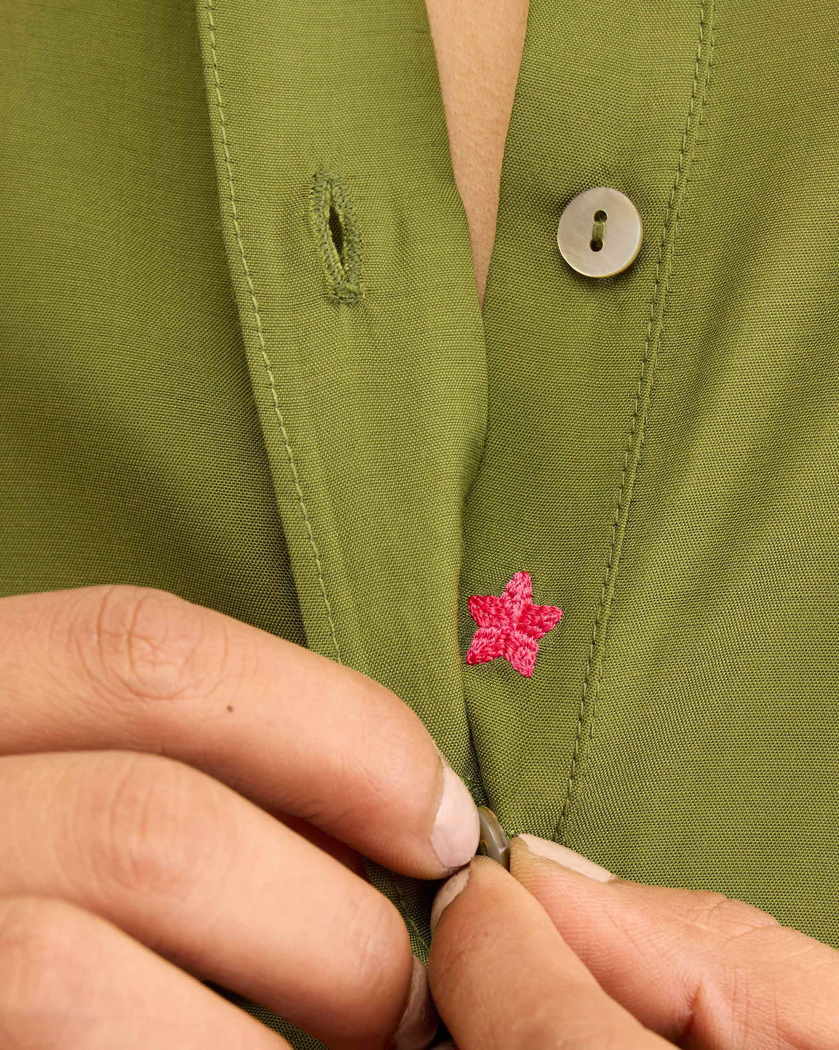 Close-up of a pink star embroidery on the placket of an olive kurta.