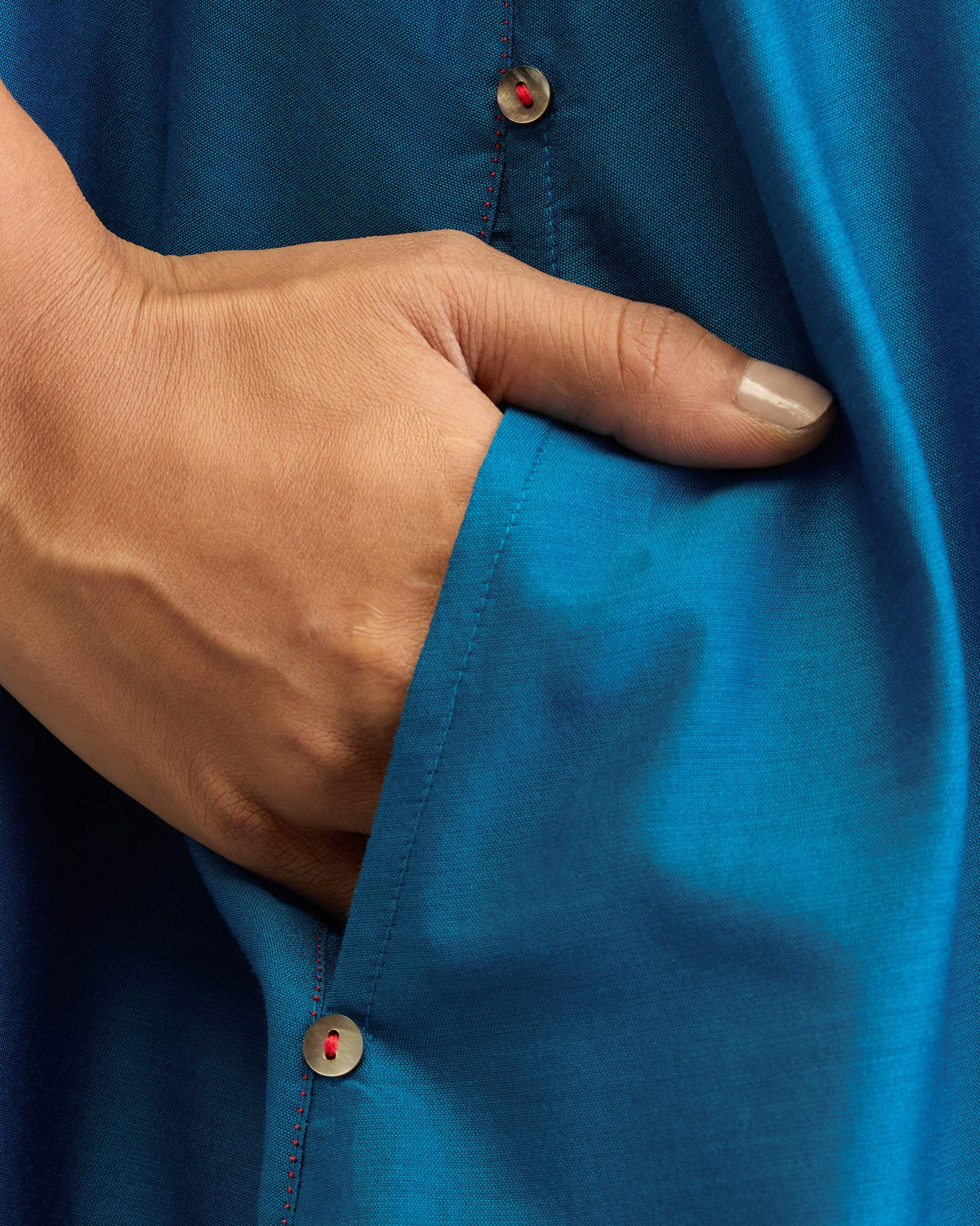 Close-up of a sapphire Double Layer Dress pocket with red-stitched buttons.