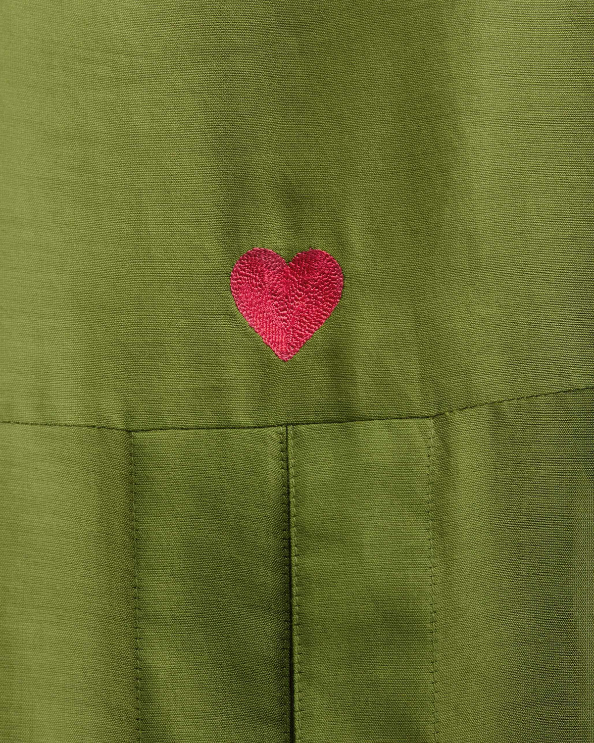 Close-up of a pink heart embroidery on an olive Cirrus shirt.