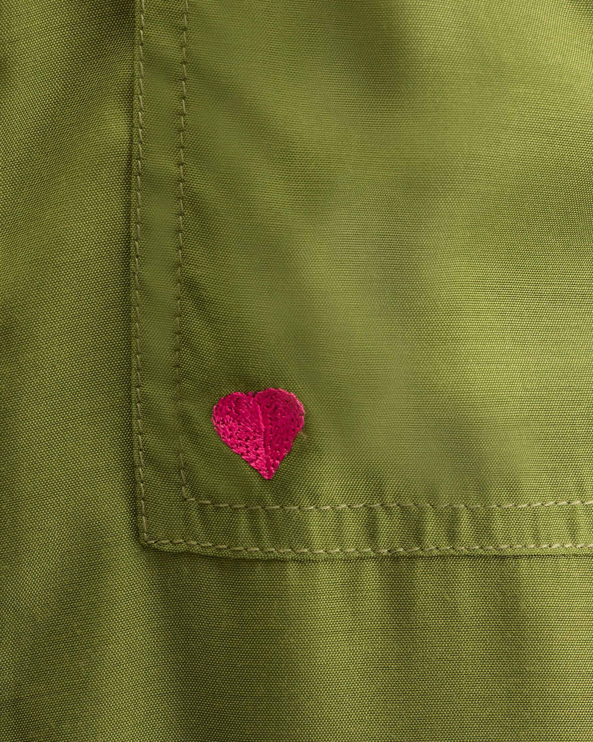 Close-up of olive Serene pants showing a pink embroidered heart on the pocket.