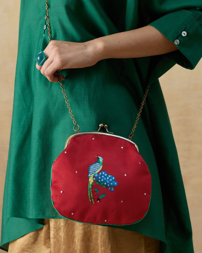 Red embroidered sling clutch with a blue bird motif held by a chain strap.