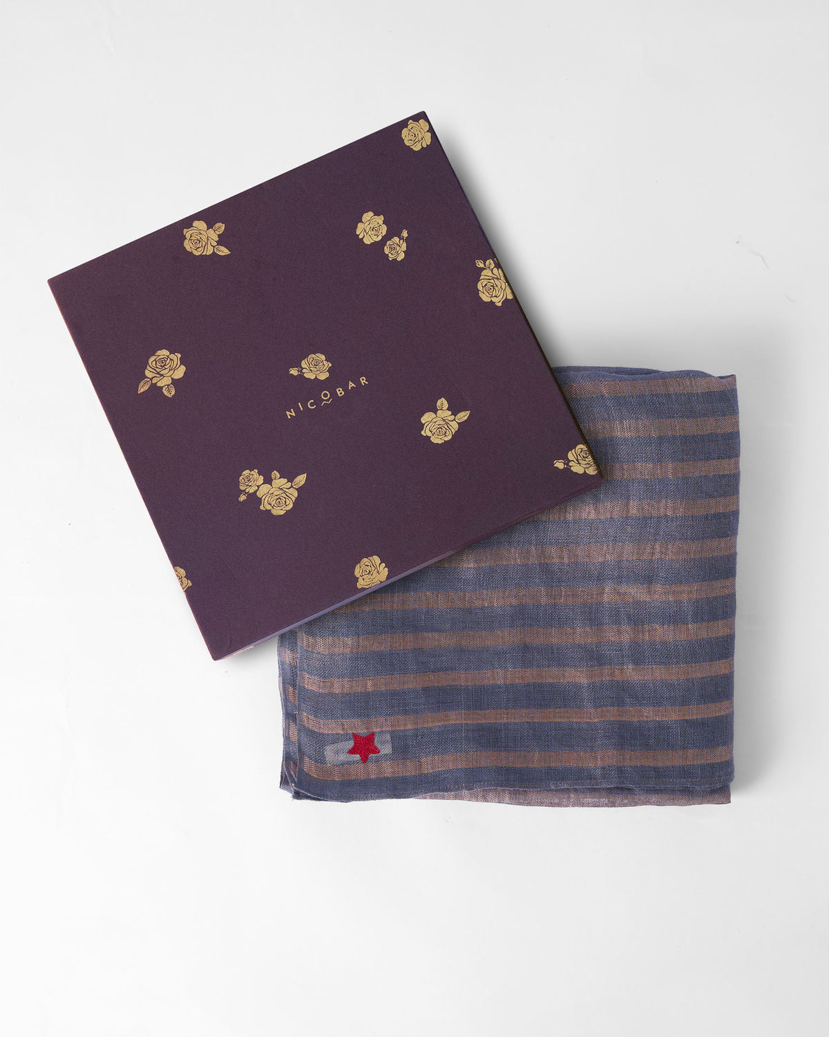 Firefly Scarf in grey and gold folded beside a purple gift box.