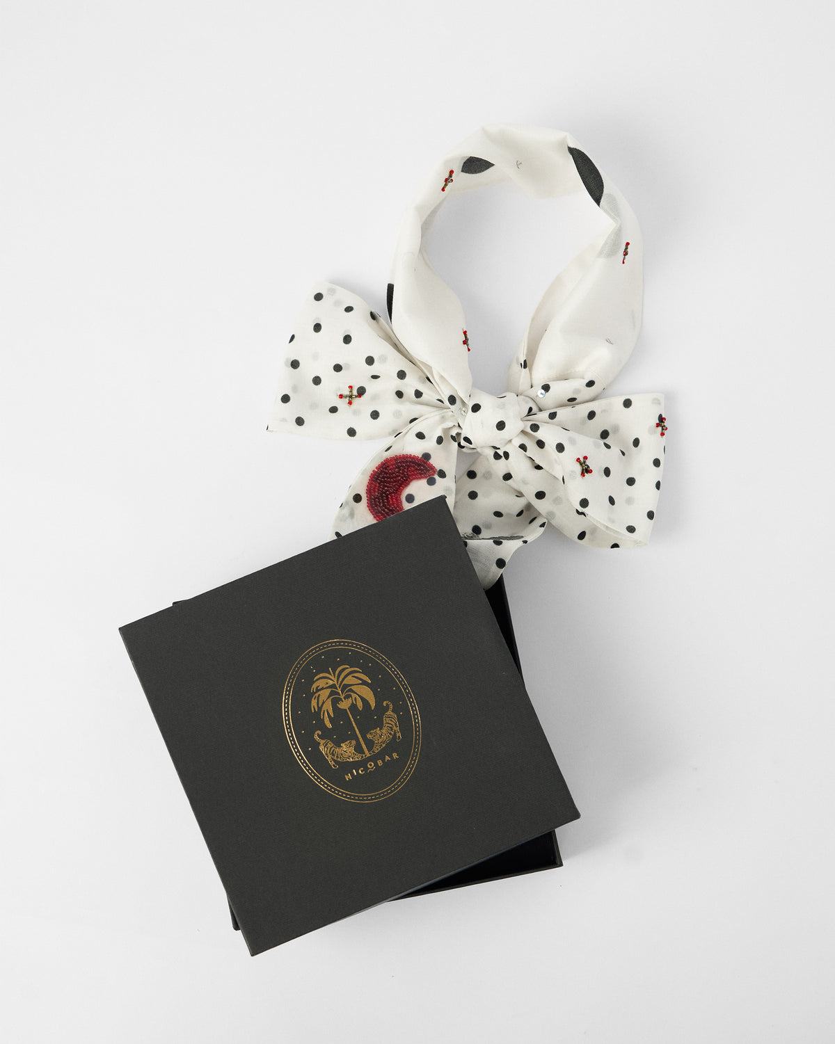 Ivory polka-dot scarf bow rising from a black Nicobar gift box.