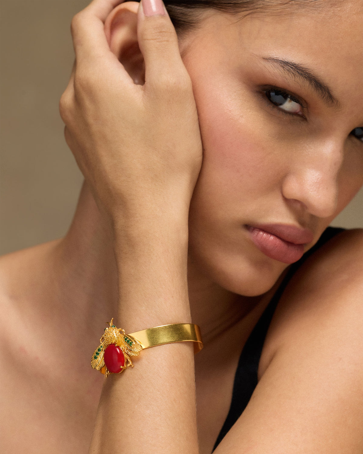 Person wearing a gold Bug bracelet with a red stone insect motif.