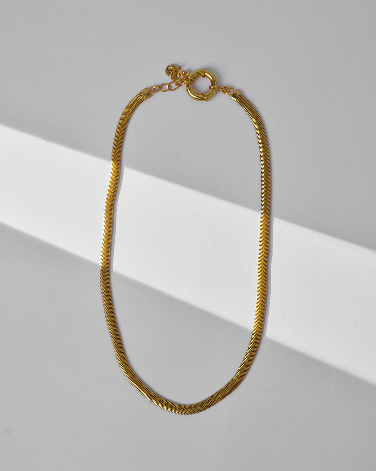 Gold herringbone chain laid flat with clasp and extender.