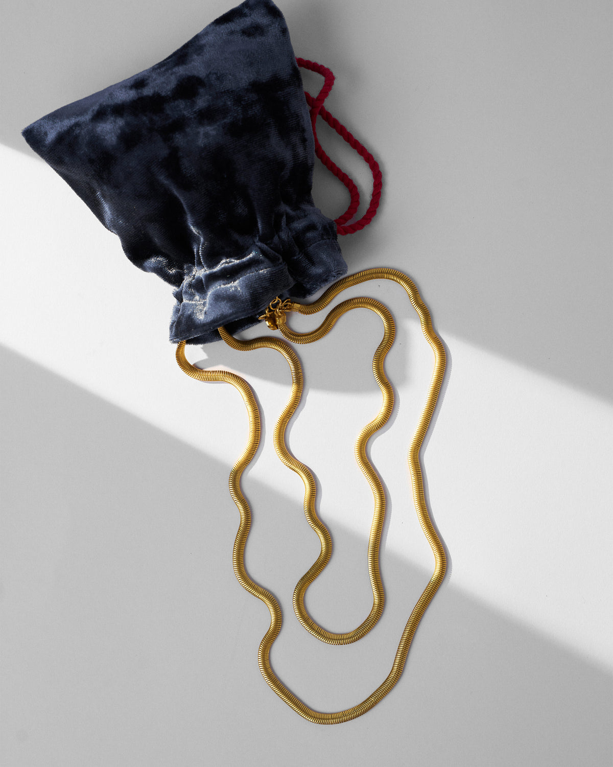 Gold Layered Herringbone Chain laid out beside a navy velvet pouch.