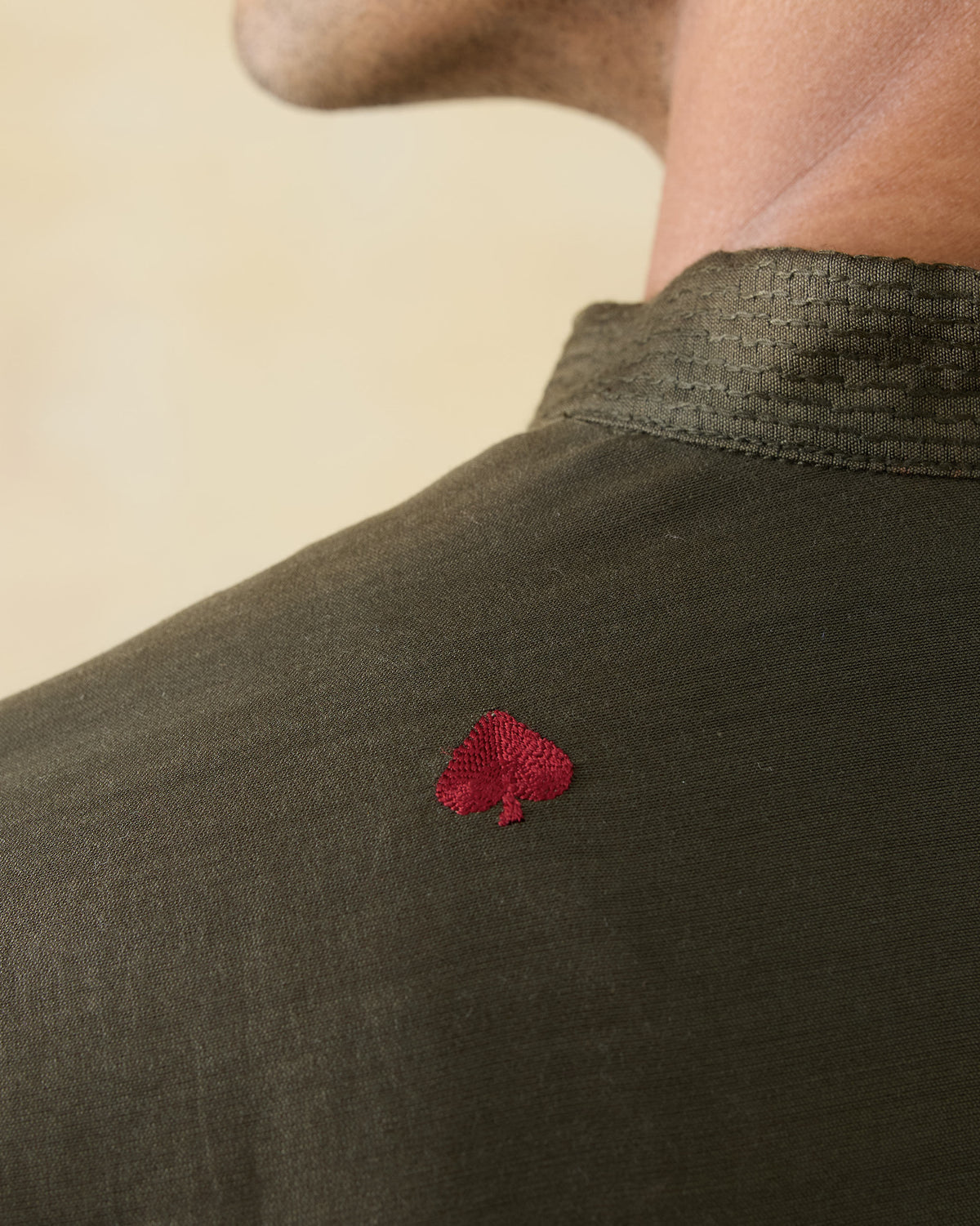Close-up of a red embroidered mark on the back of an olive green Neckband Kurta.