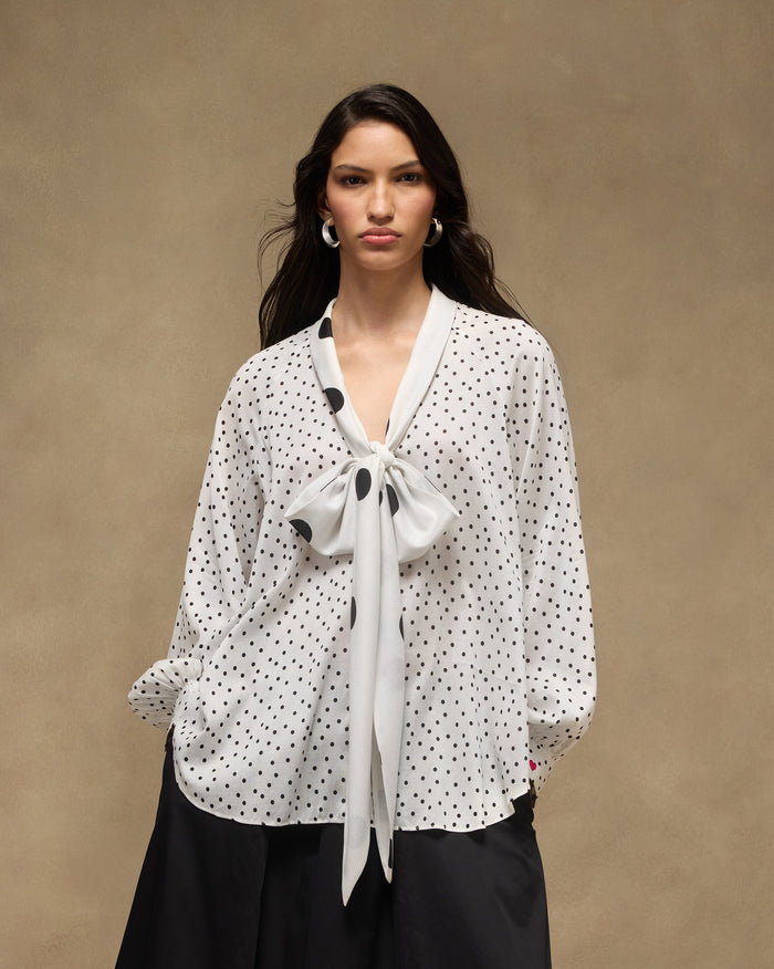 Person wearing an ivory and black polka-dot Whirl tie-up top with a large bow.