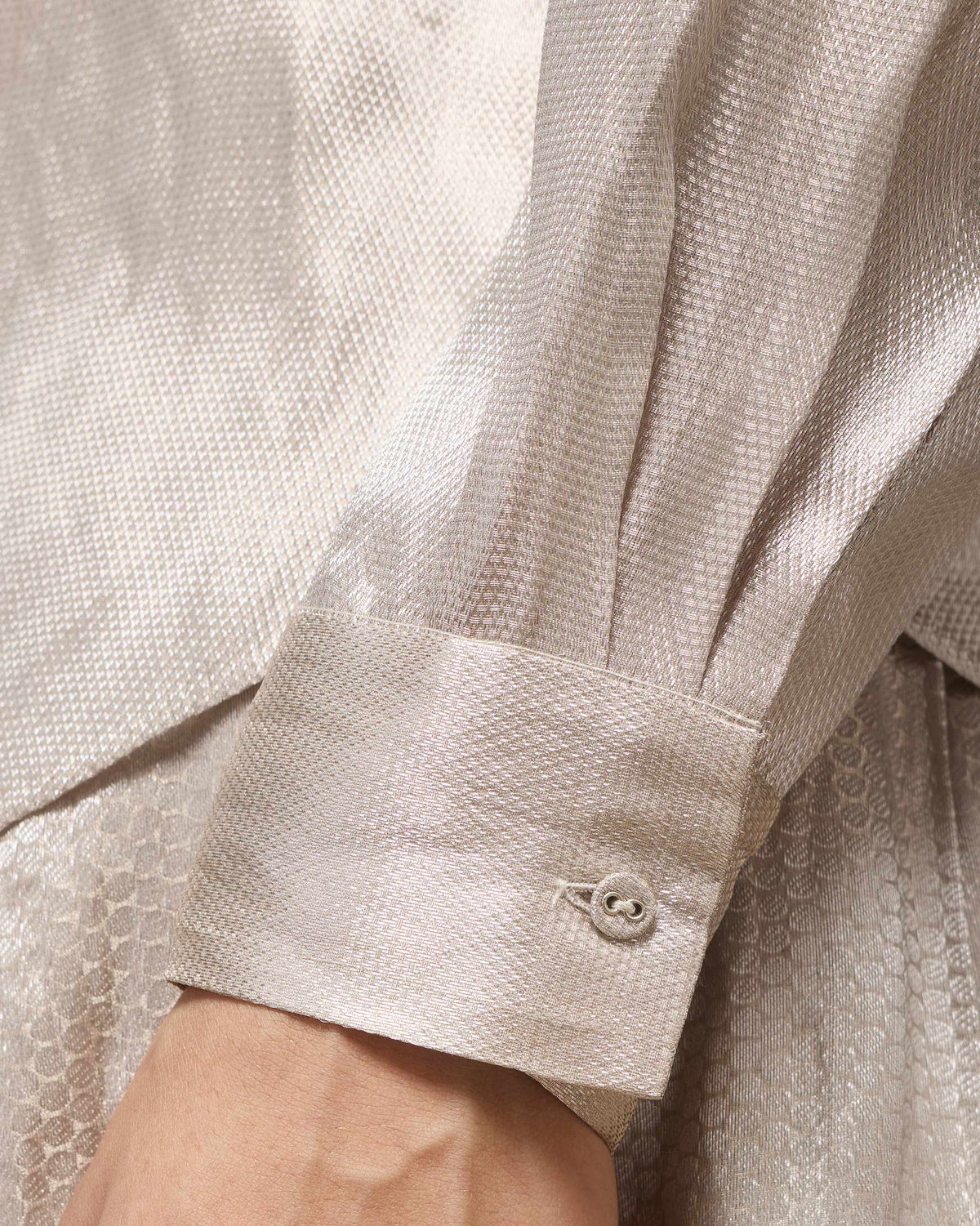 Close-up of a silver tissue organza shirt cuff with a matching button.