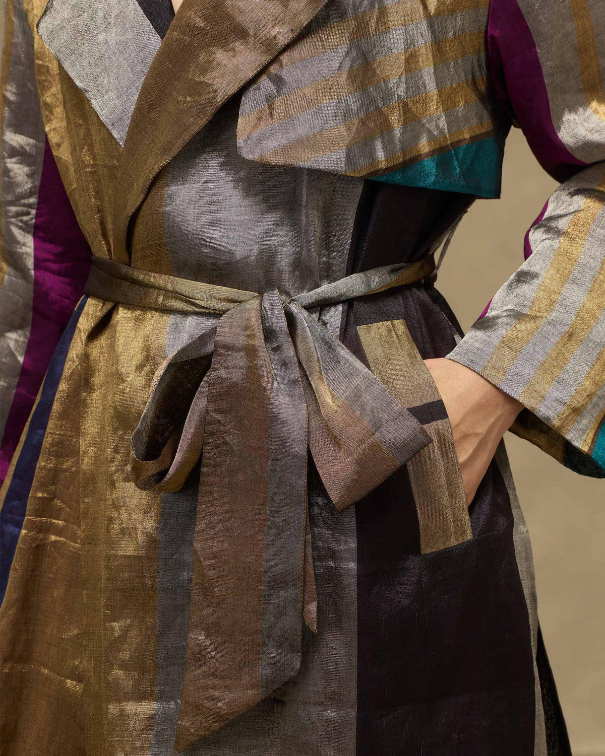 Close-up of a metallic striped trench with a fabric belt and side pocket.