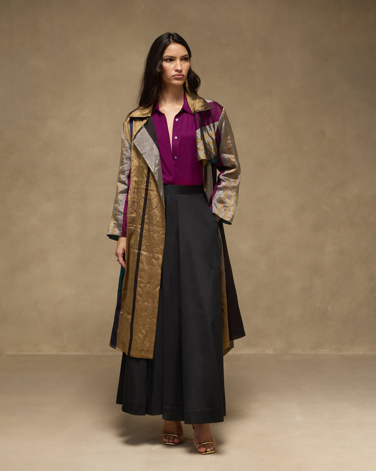 Person wearing a multicolour metallic trench coat with gold and purple panels.