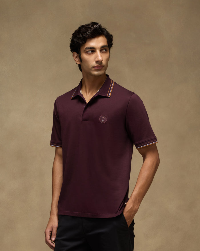 Person wearing a maroon Stag Polo with striped collar and cuff tipping.