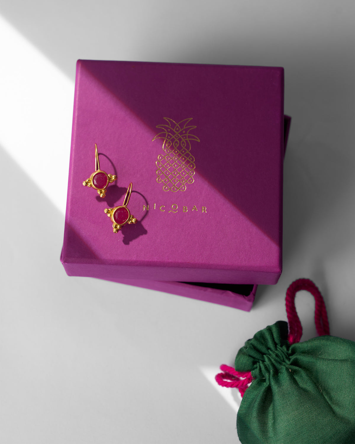 Pair of gold Pink Jade Drops on a pink gift box beside a green pouch.