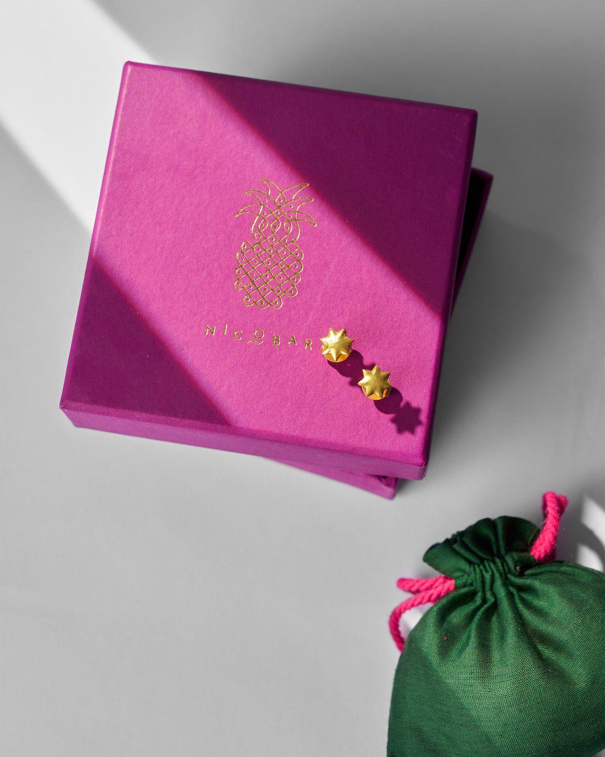 Pair of gold Sitara Studs displayed on a magenta Nicobar gift box.