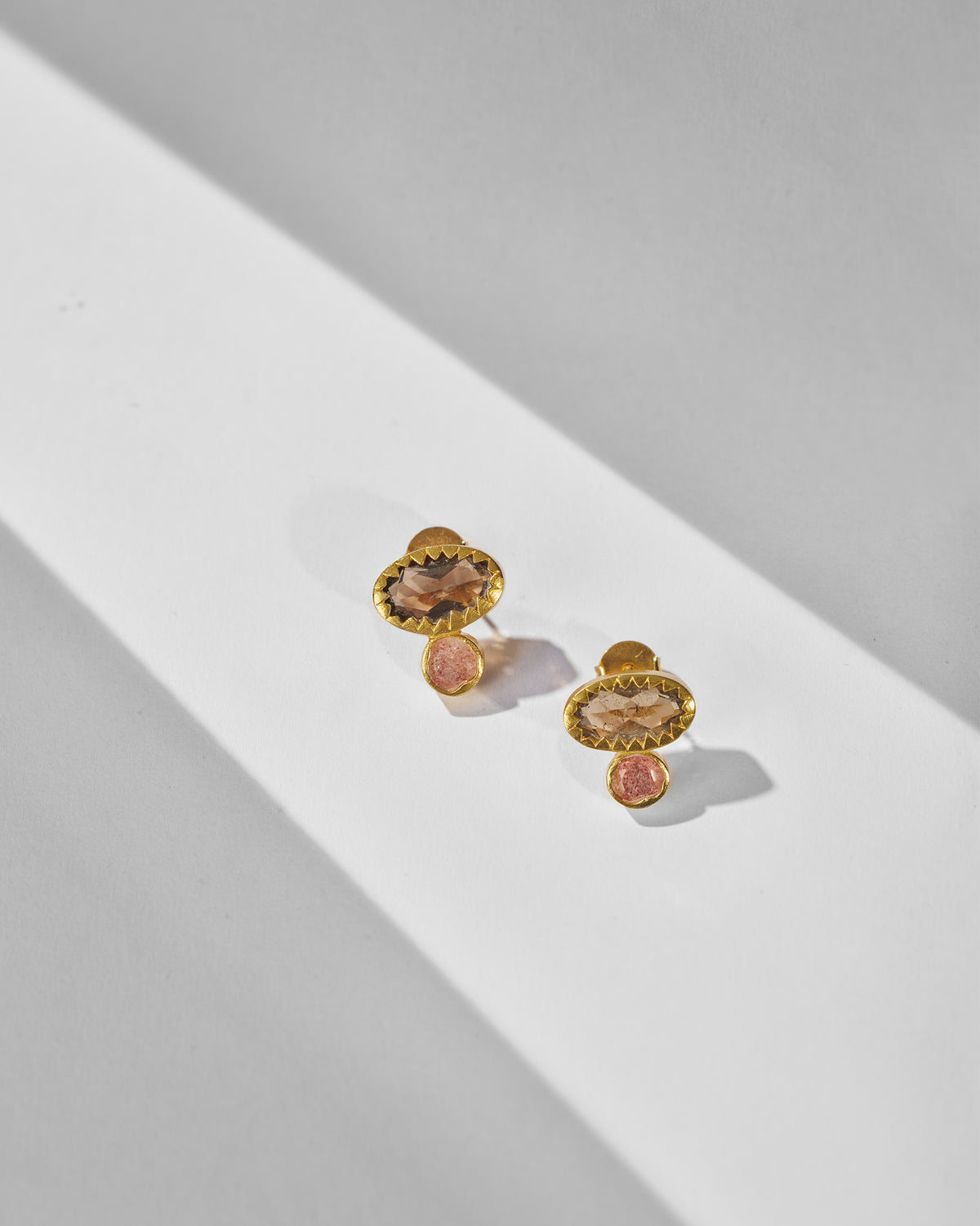 Pair of Coastline Earrings laid flat, with brown stone tops and pink stone drops.