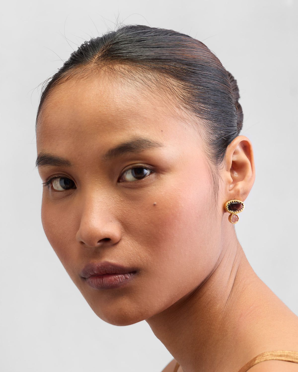 Person wearing Coastline Earrings, with brown stone tops and pink drops.