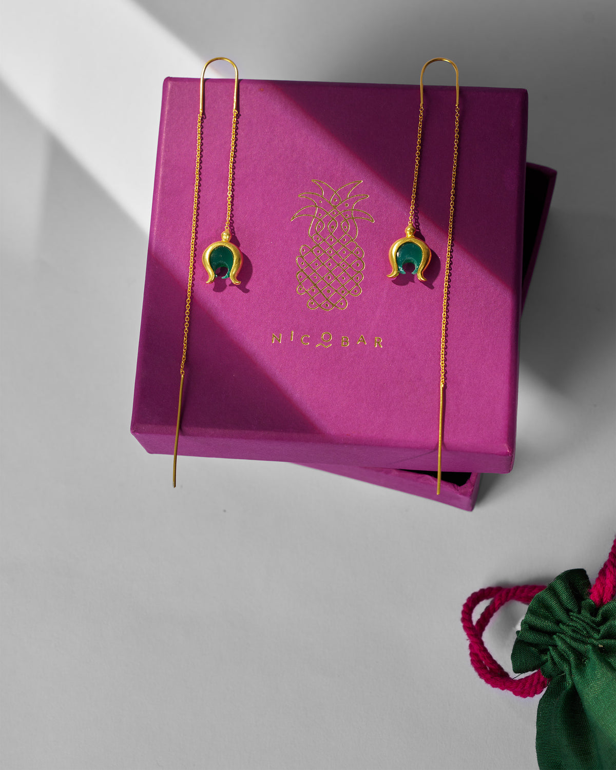 Gold Chandphool sui dhaga earrings on a magenta Nicobar gift box.
