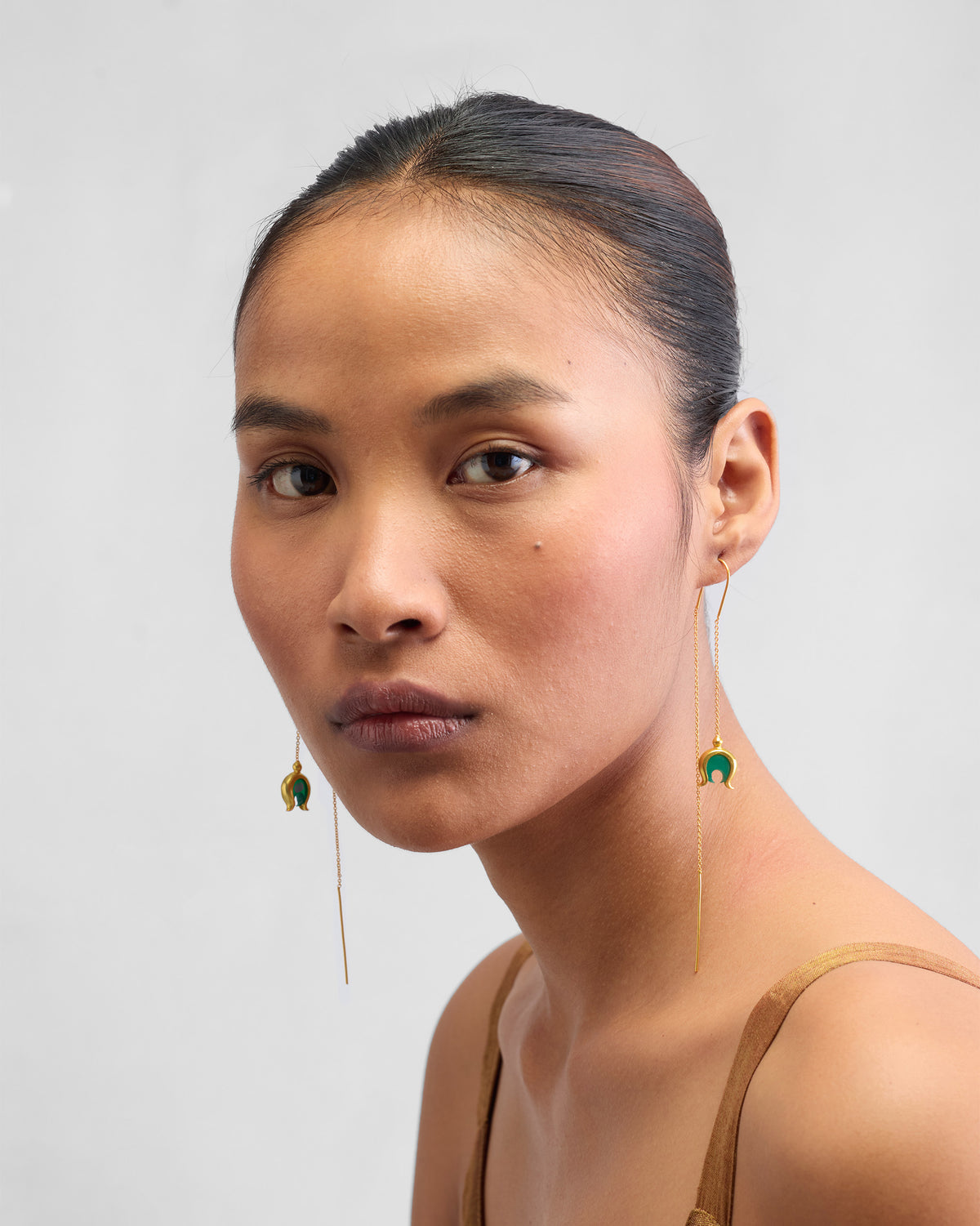 Person wearing gold Chandphool sui dhaga earrings with green onyx drops.