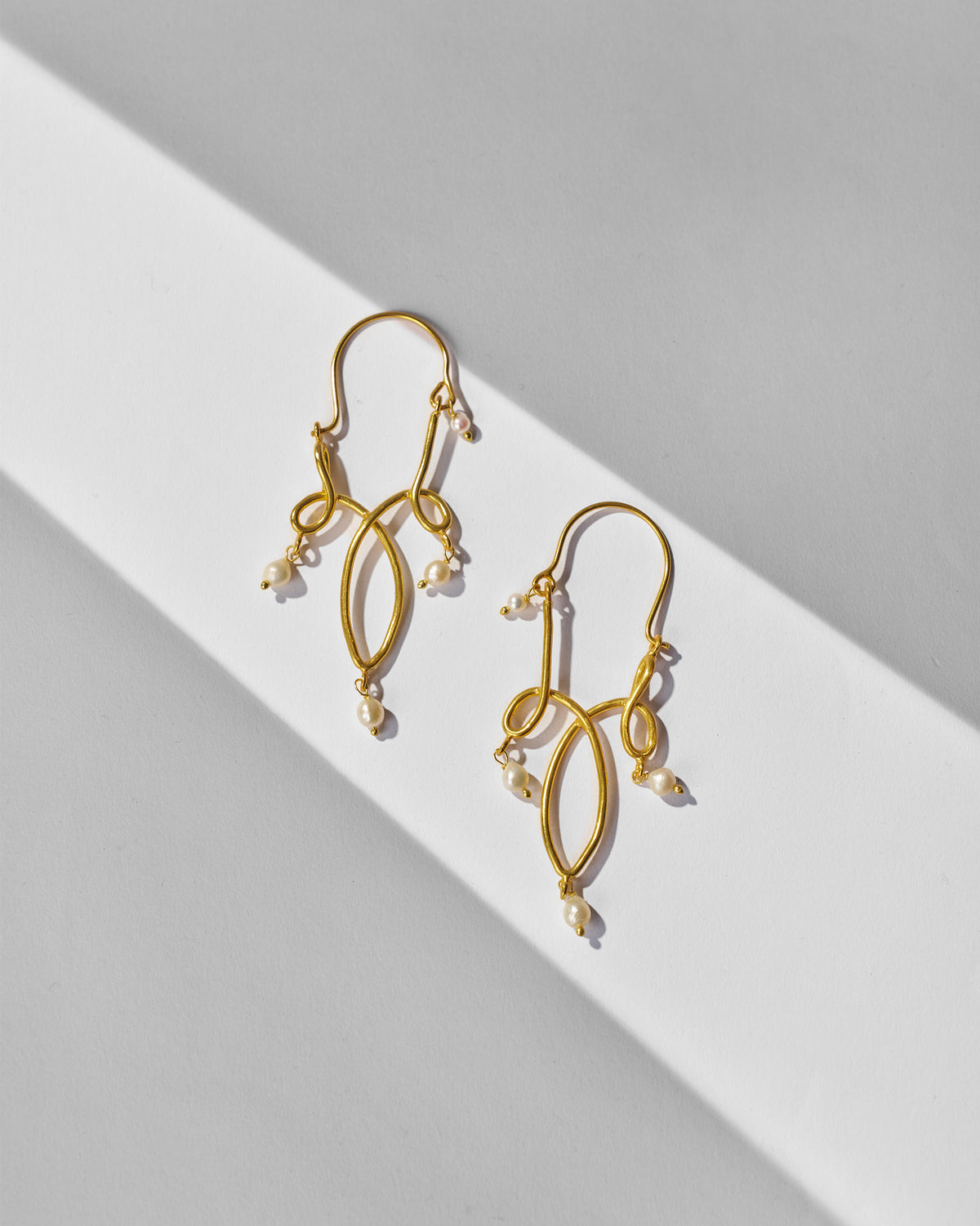 Pair of gold Kolam balis with pearl drops laid flat.
