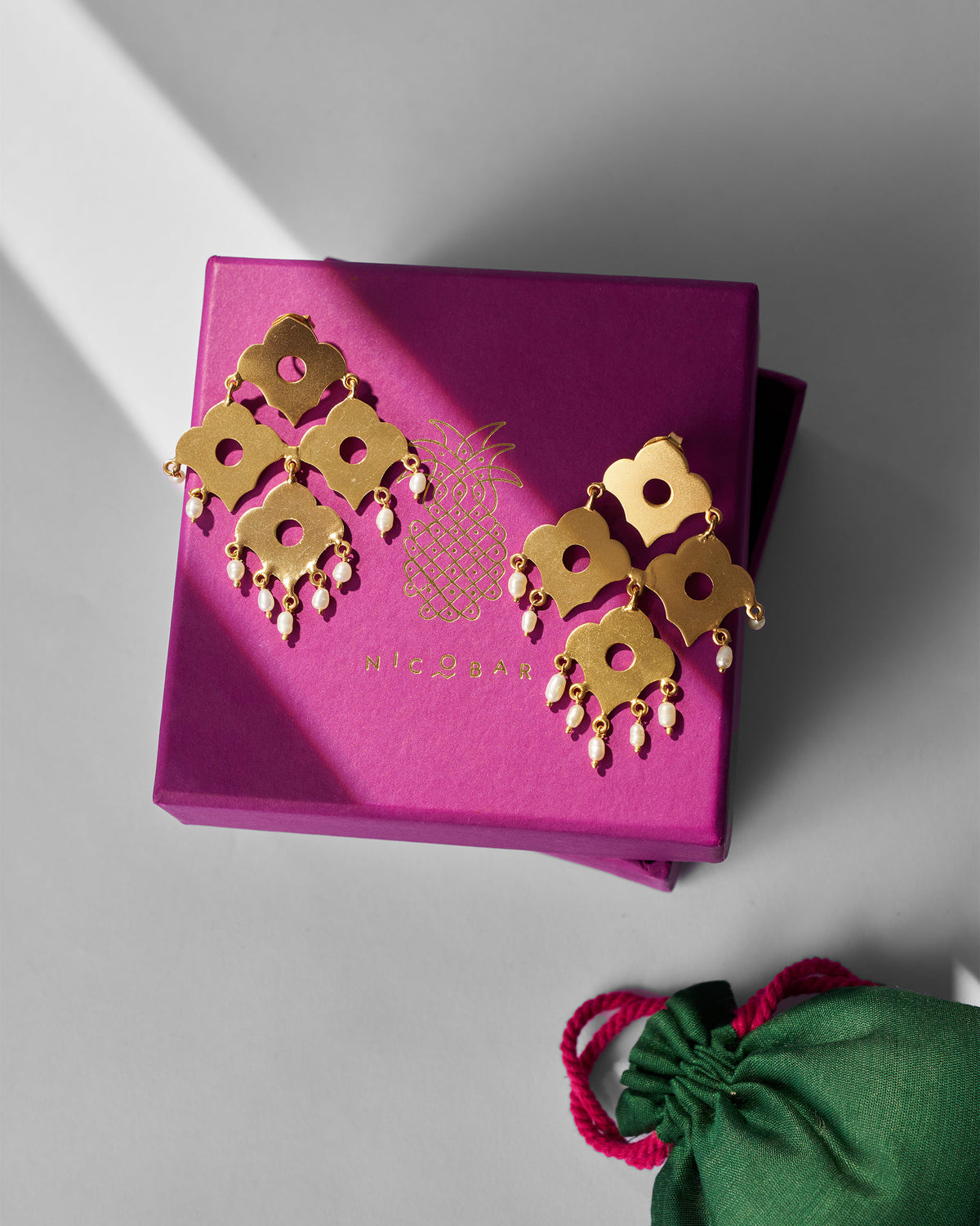 Pair of gold Phool Jaal Earring on a pink gift box beside a green pouch.