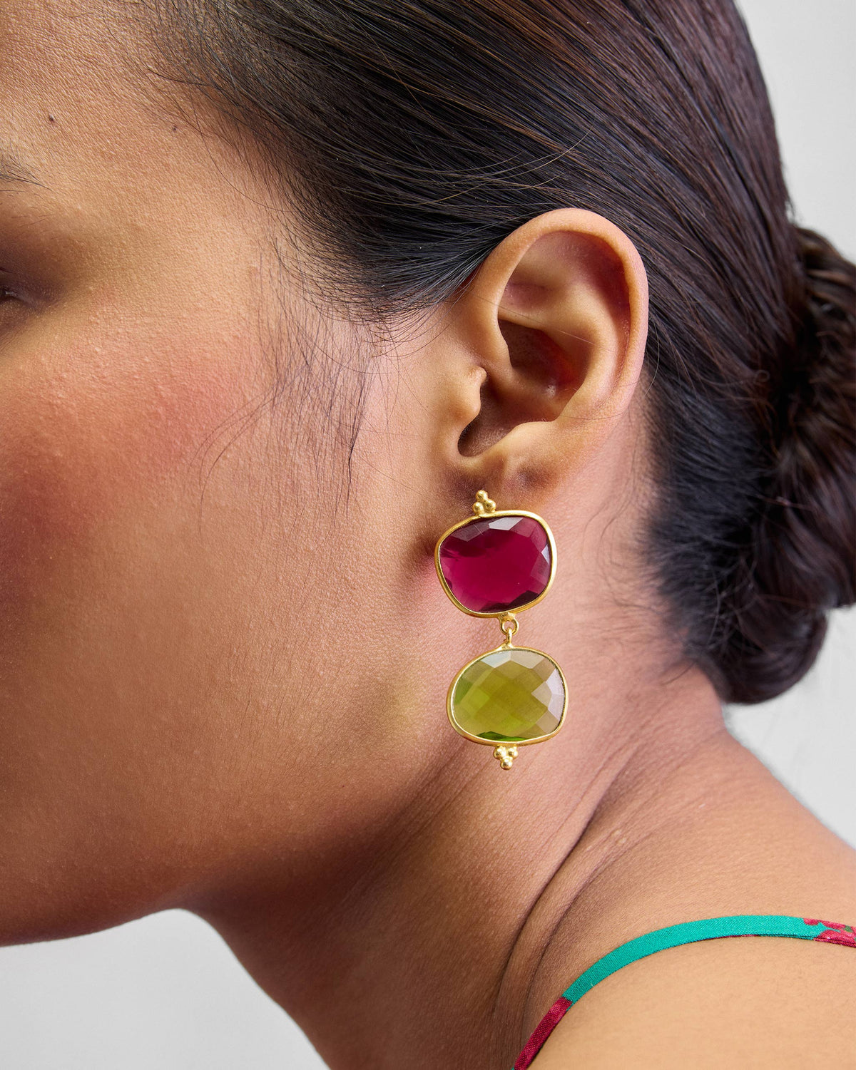 Side view of gold Nadi Earrings worn on a person, with pink and green stones.