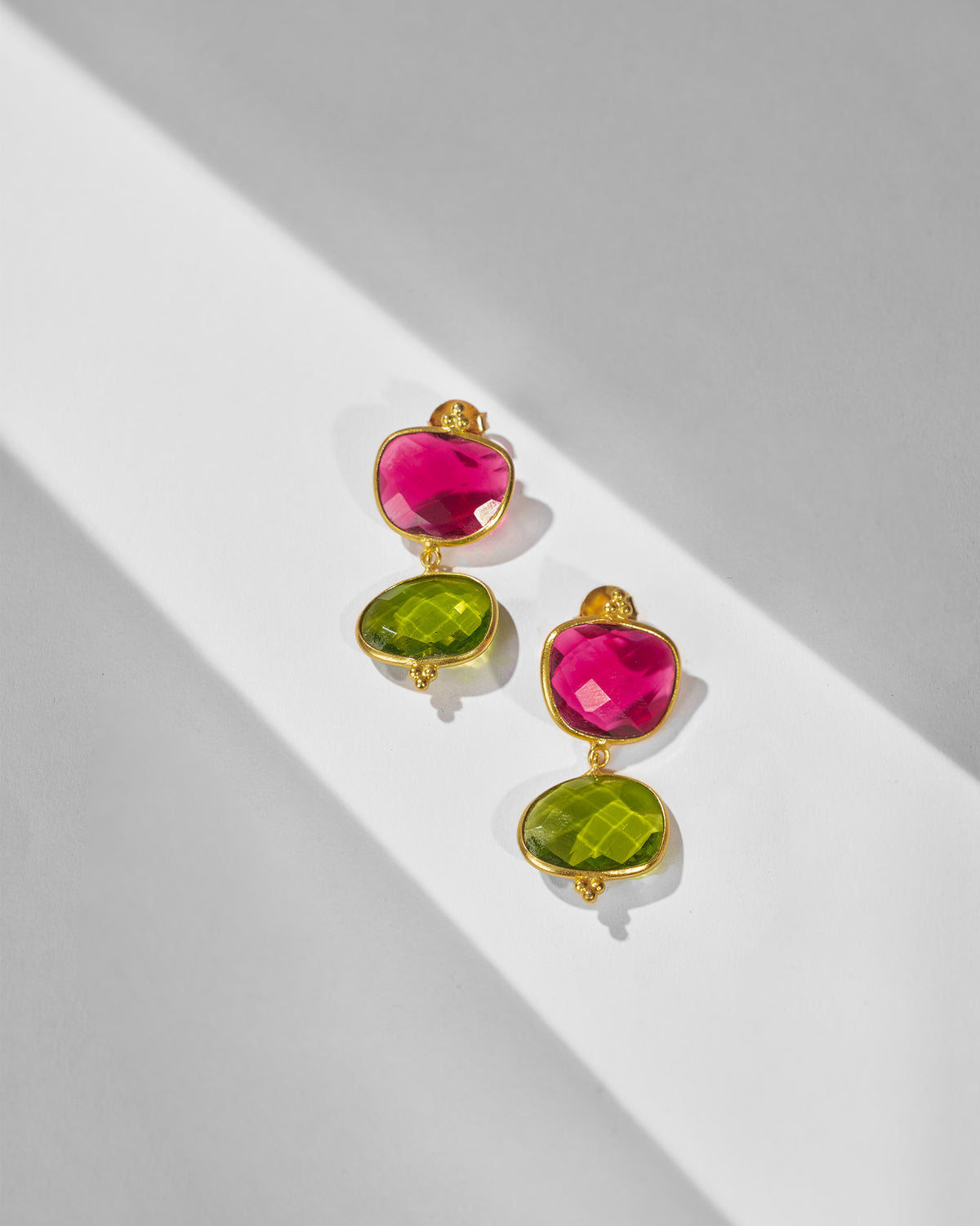 Pair of Nadi Earrings with pink and green stones laid flat.
