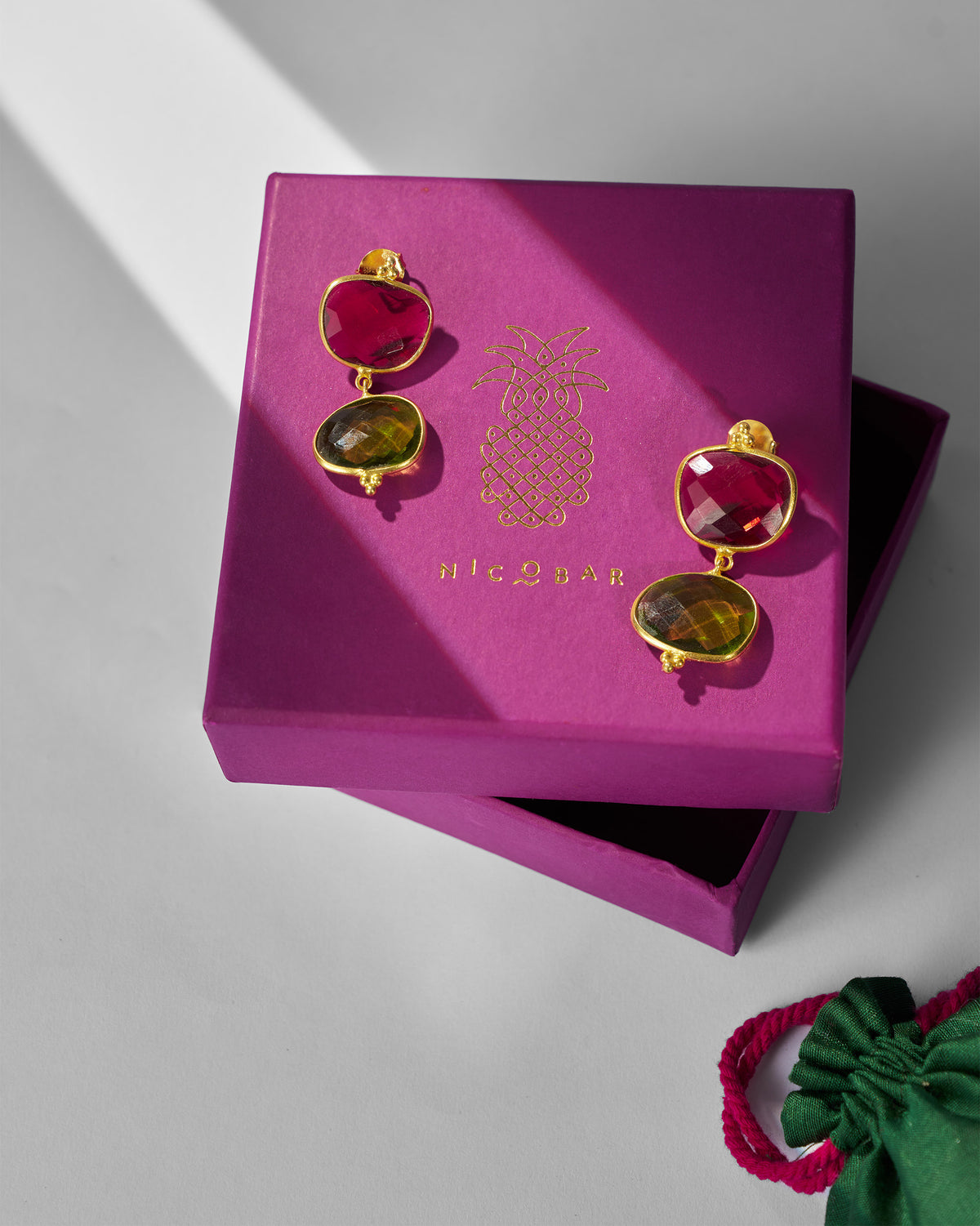 Pair of Nadi Earrings on a pink gift box beside a green pouch.