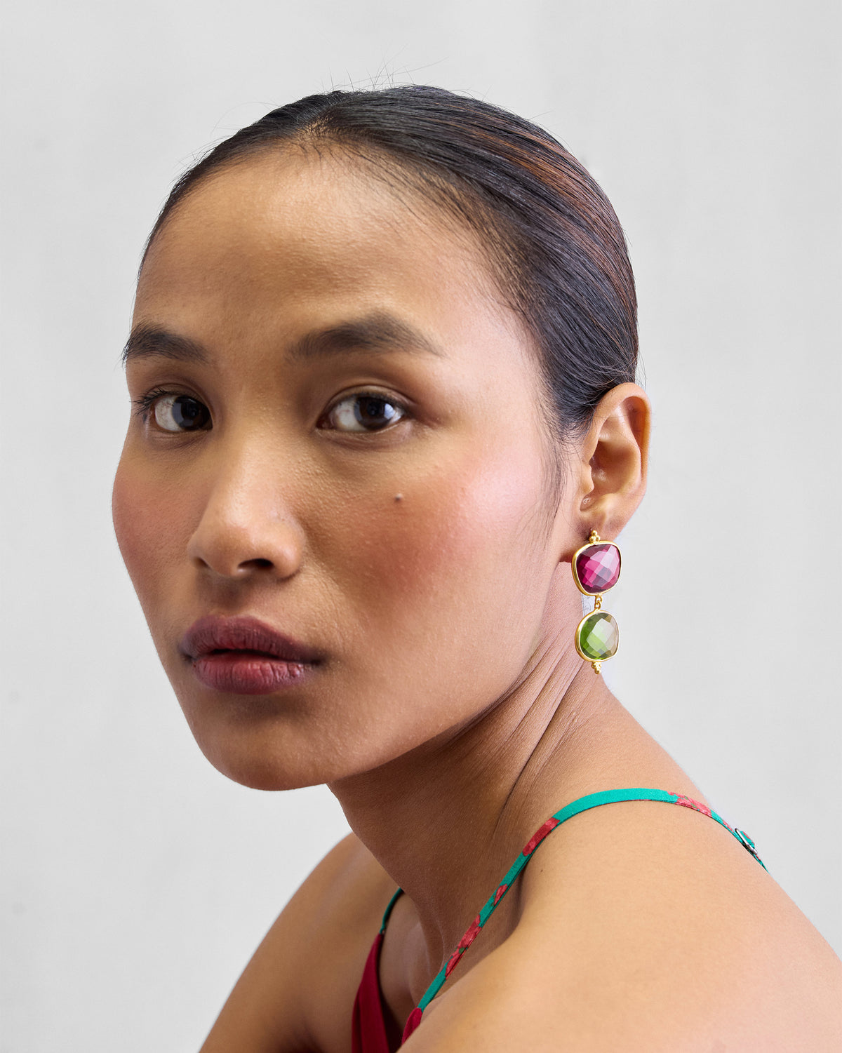 Person wearing gold Nadi Earrings with pink and green stones.