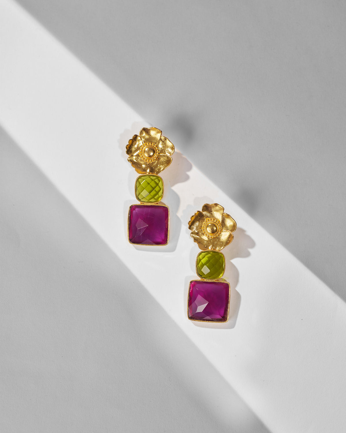 Pair of gold dessert rose drops with green and magenta stones laid flat.