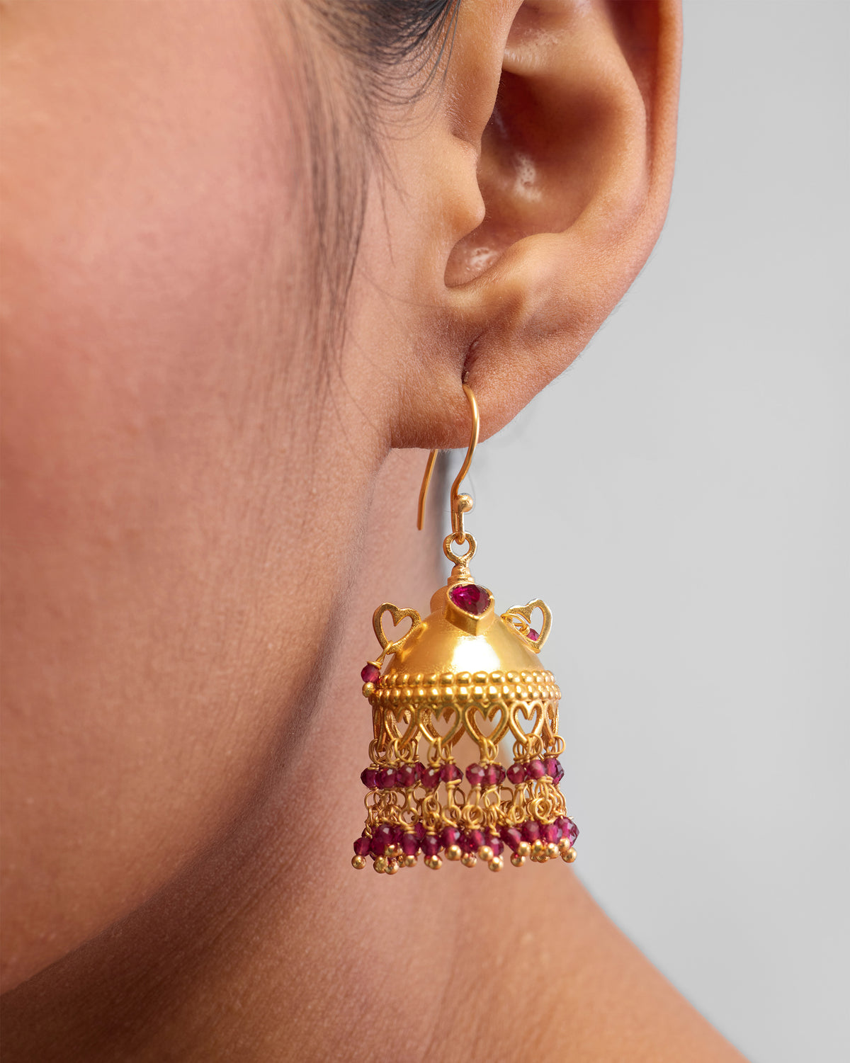 Close-up of a gold Kaveri jhumka with red bead fringe.