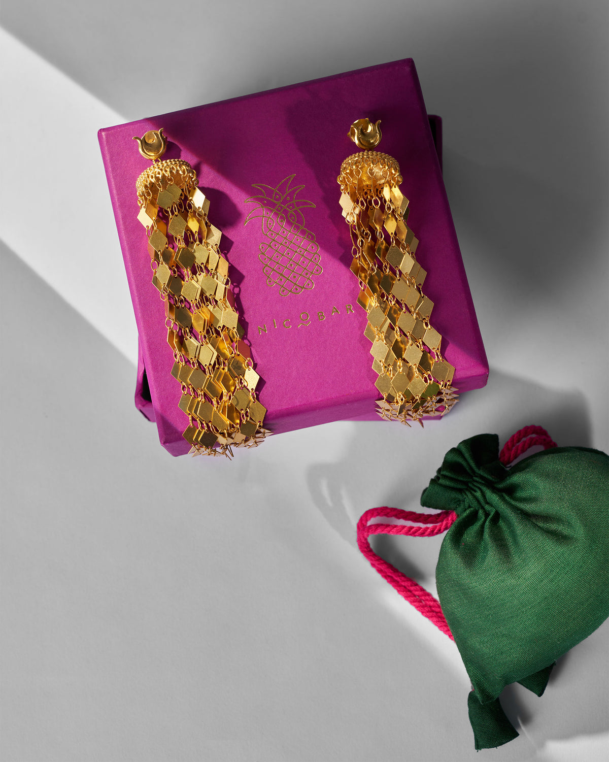 Gold Gulbahar earrings on a magenta Nicobar box with a green pouch.