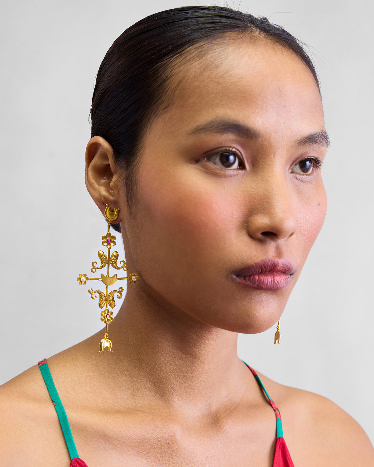 Person wearing a long gold gul baag earring with fish and flower motifs.