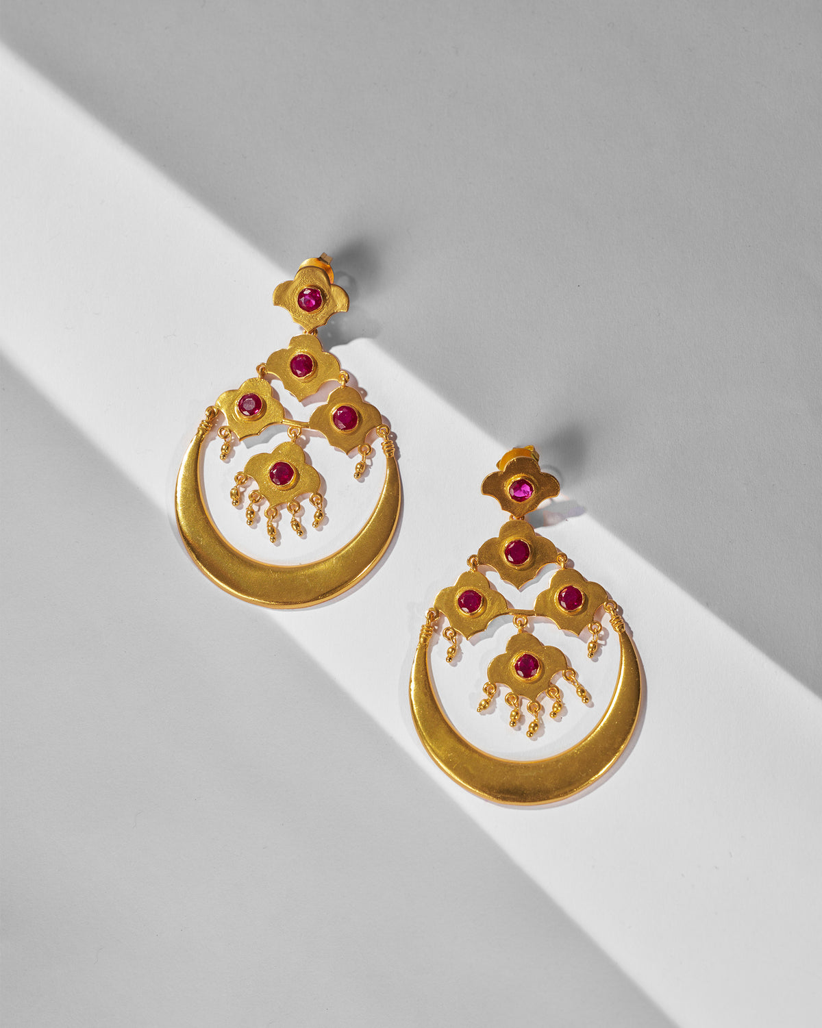 Pair of gold Moon Flower earrings with red glass laid flat.