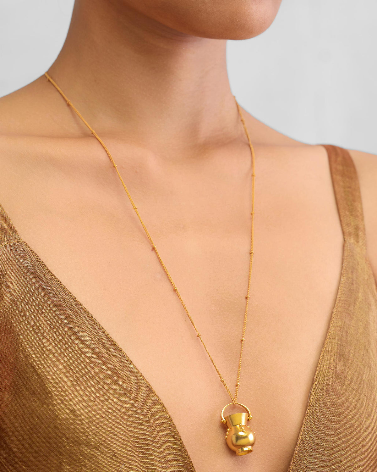 Person wearing a long gold Sage necklace with a pot pendant.