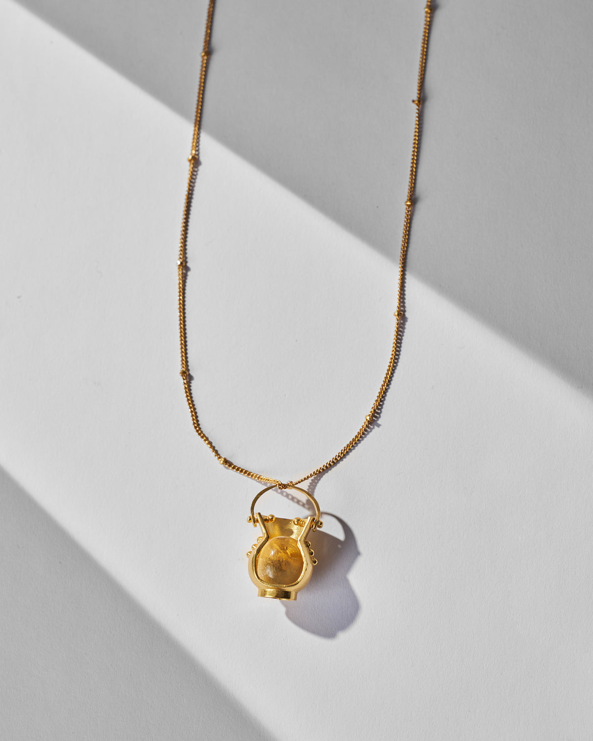 Close-up of the gold Sage pot pendant with an amber stone.