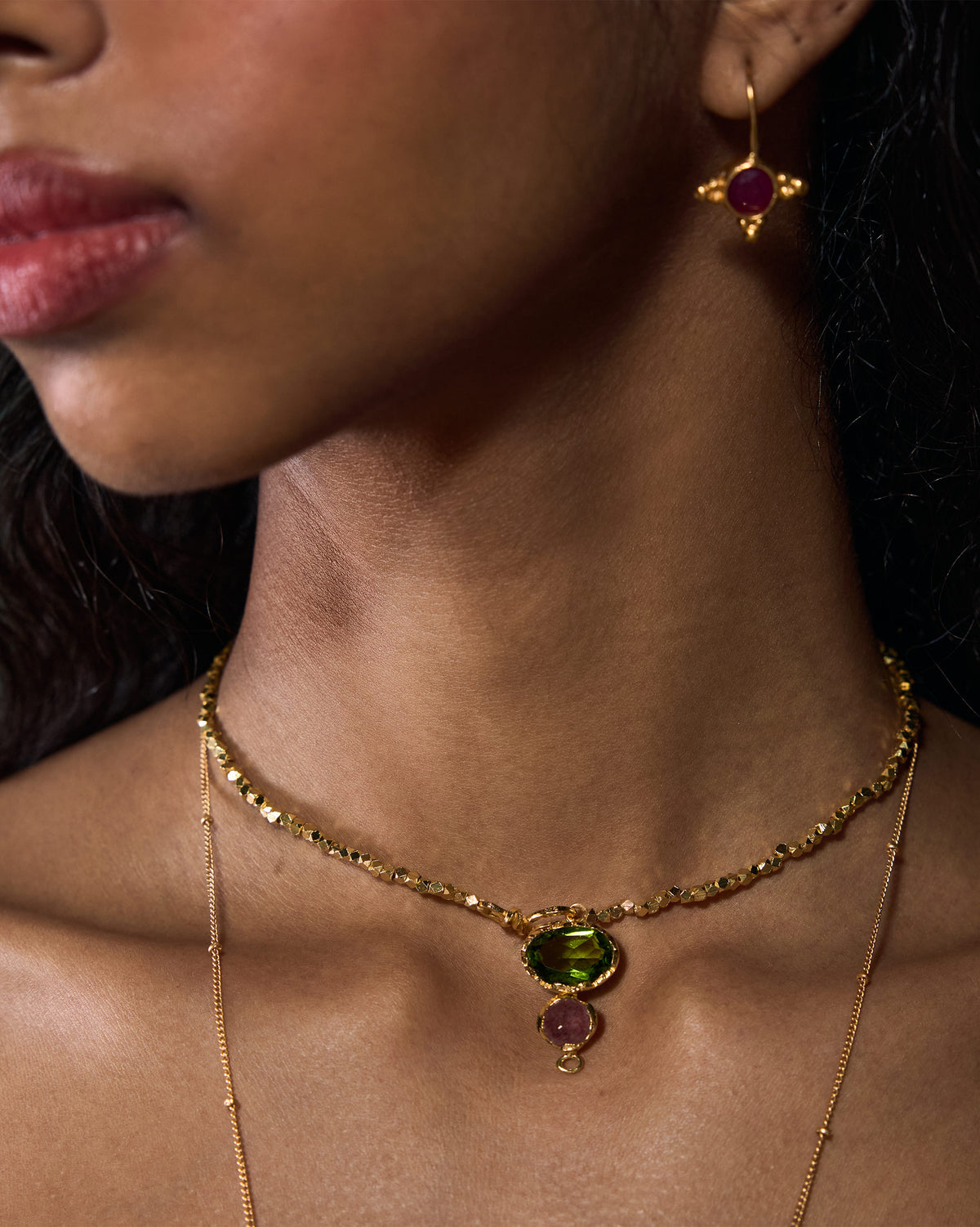 Close-up of a gold Kari necklace with green and pink stones worn on a person.