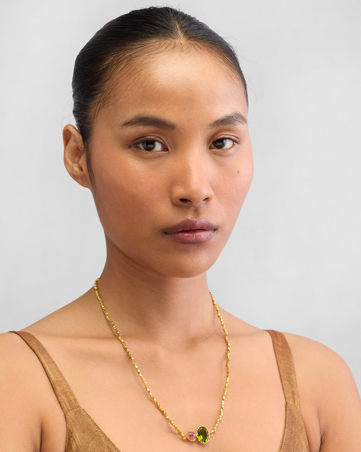 Person wearing a gold Kari necklace with green and pink stones.