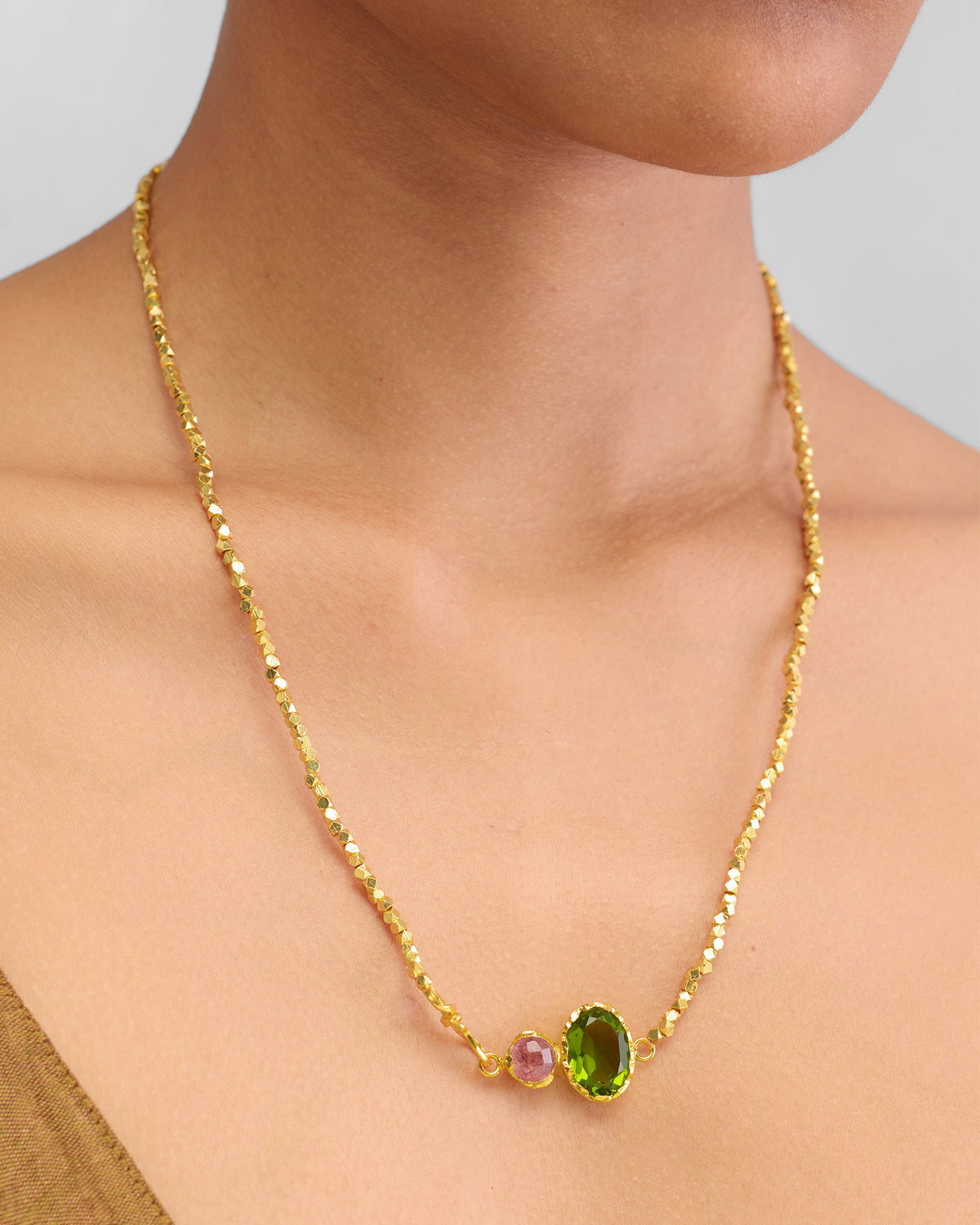 Close-up of a gold Kari necklace with green and pink stones at the neck.