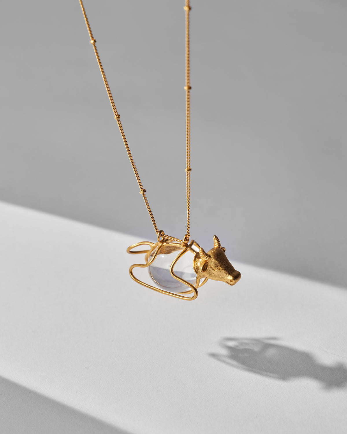 Close-up of a gold Nandi pendant with a bull head and caged clear bead.