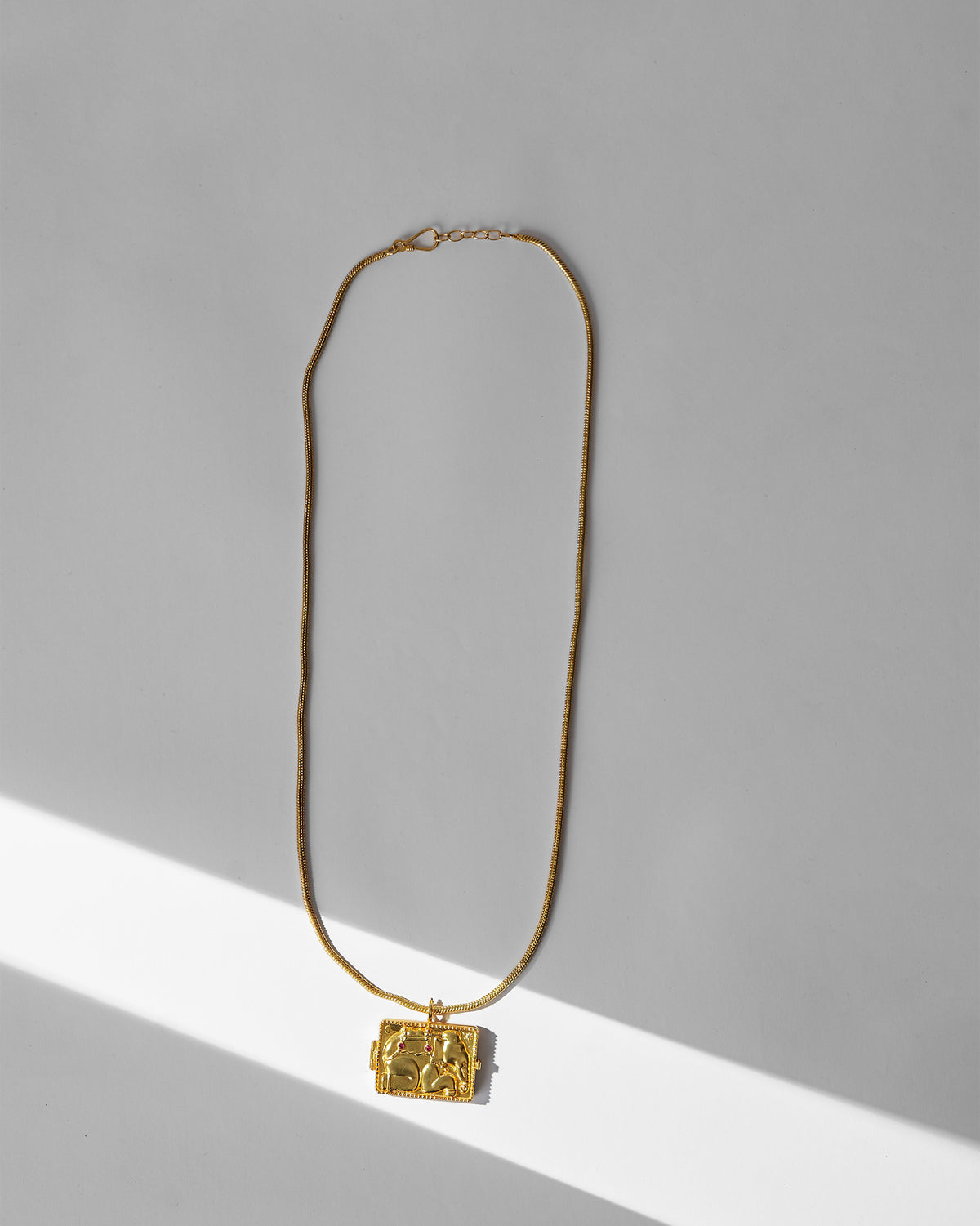 Gold Appu necklace with a rectangular elephant-relief locket on a snake chain.