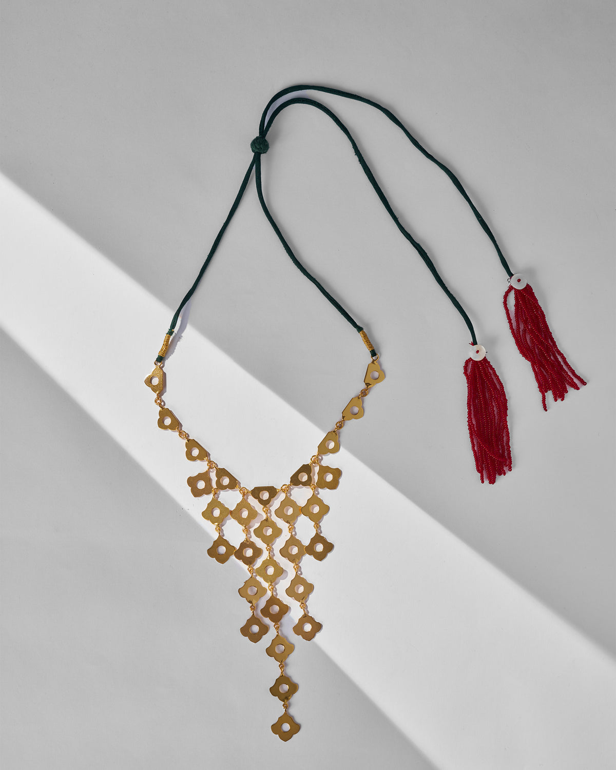 Gold Phool Jaal necklace laid flat on a green cord with red tassels.