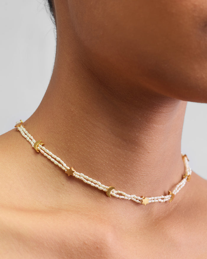 Gold Bindu pearl necklace with star and crescent charms worn at the neck.
