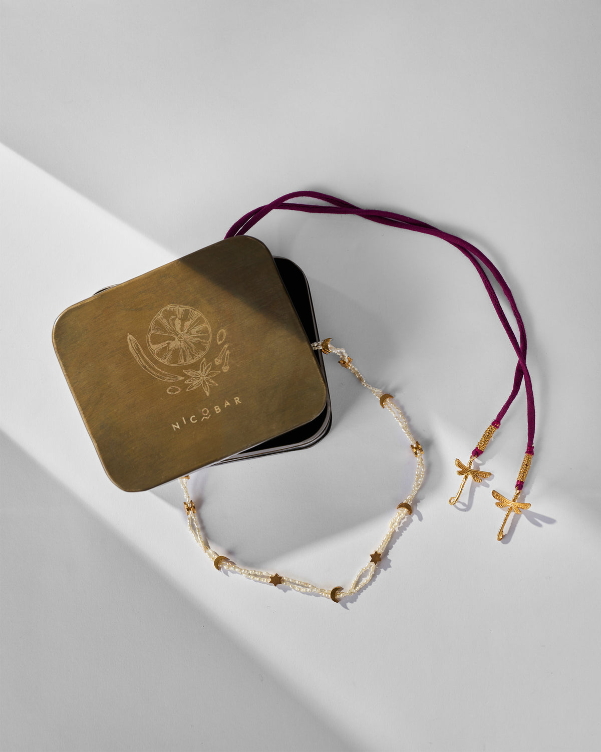 Bindu pearl necklace draped around a brass Nicobar jewelry tin.