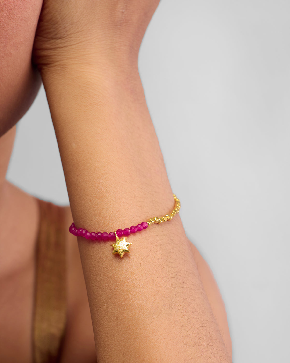 Person wearing a Sitara Bracelet with pink beads and a gold star charm.