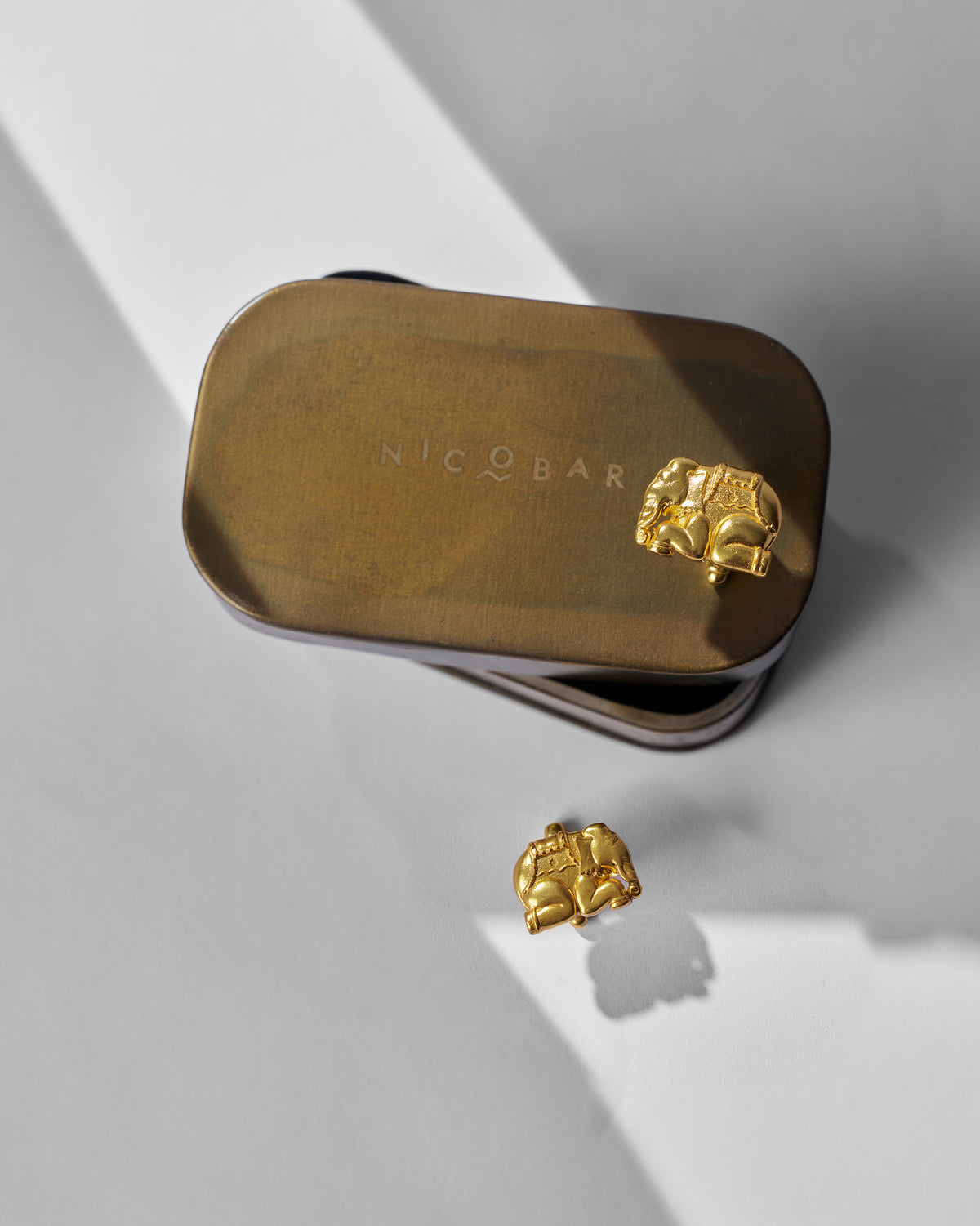 Appu Cufflinks on a gold tin, with another beside it on white.