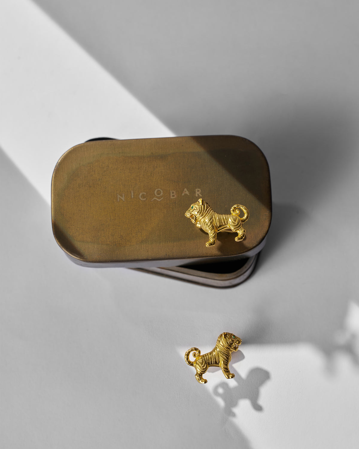 Roar Cufflinks with gold tiger motifs placed on and beside a Nicobar tin.
