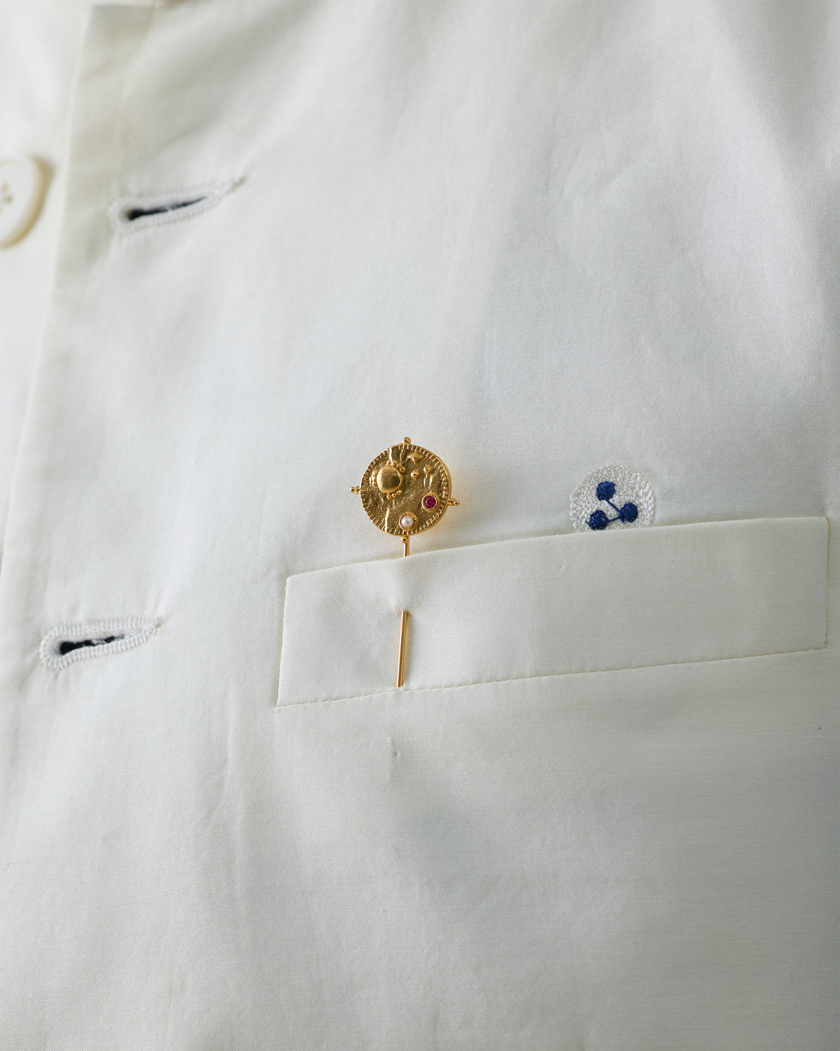 Gold Nebra Lapel Pin with a red stone pinned to a white shirt.