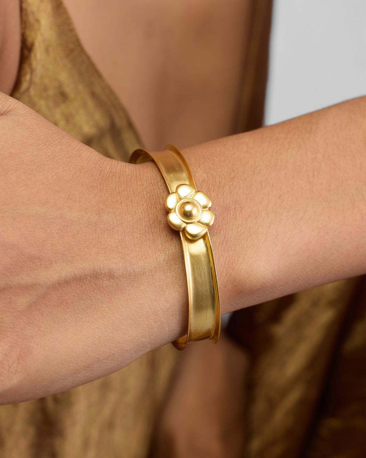 Person wearing Clover Cuff, a wide gold cuff with a raised flower motif.